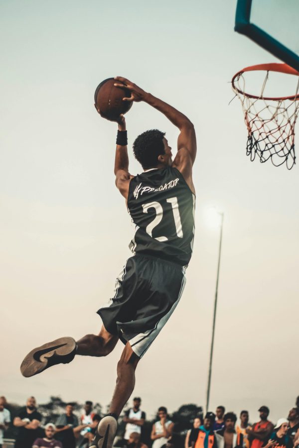 A dynamic basketball player executing a slam dunk during a vibrant outdoor game. They get the suits in best Jersey Store.